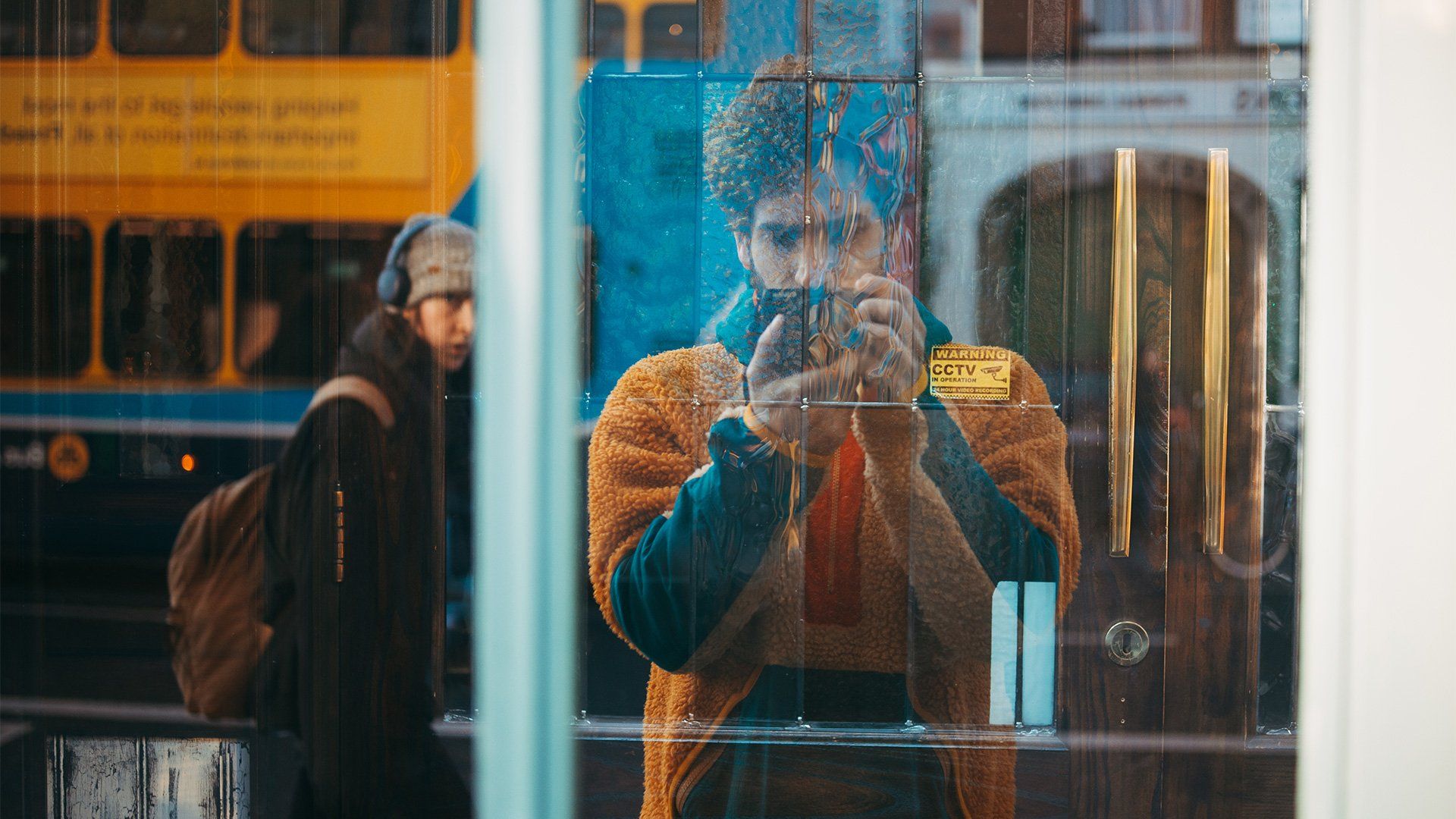 Giuseppe taking a photo of a shop window, showing passers by in the reflection.
